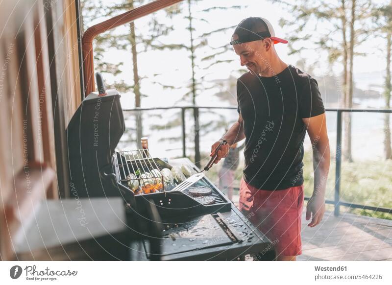 Mann kocht auf dem Grill, während er auf der Terrasse steht Farbaufnahme Farbe Farbfoto Farbphoto Außenaufnahme außen draußen im Freien Menschen Personen