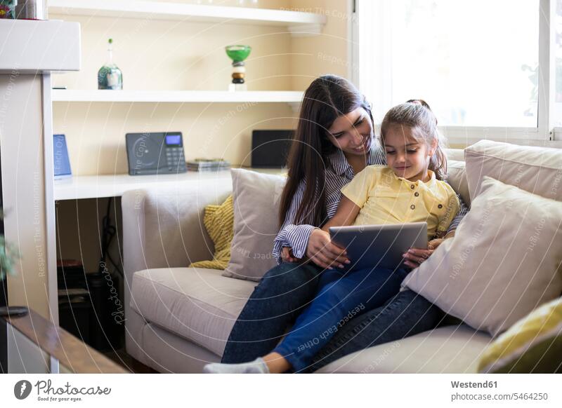 Glückliche Mutter und Tochter sitzen auf der Couch zu Hause mit Tablette Tablet Computer Tablet-PC Tablet PC iPad Tablet-Computer Zuhause daheim glücklich