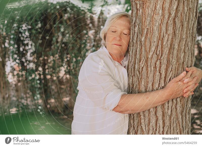 Ältere Frau mit geschlossenen Augen umarmt Baumstamm, während sie im Hof steht Farbaufnahme Farbe Farbfoto Farbphoto Spanien Freizeitbeschäftigung Muße Zeit