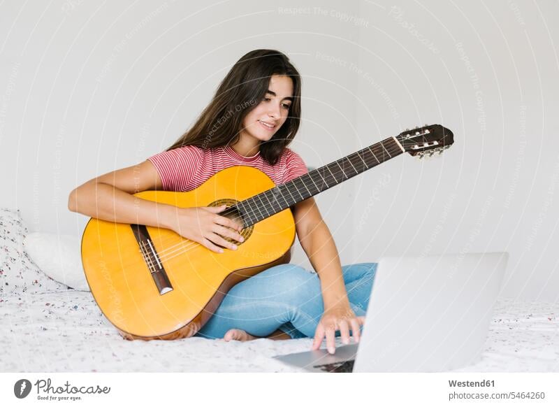 Frau lernt zu Hause im Schlafzimmer online Gitarre Farbaufnahme Farbe Farbfoto Farbphoto Innenaufnahme Innenaufnahmen innen drinnen Tag Tageslichtaufnahme