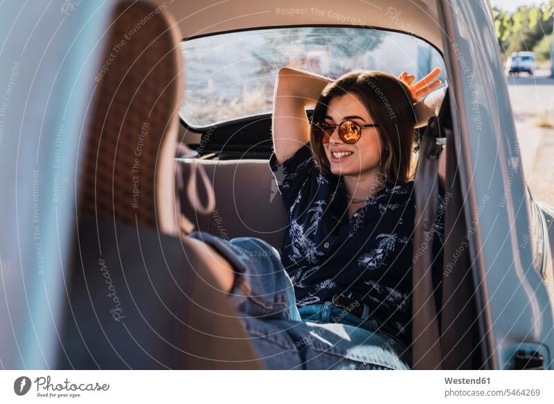 Lächelnde junge Frau mit Sonnenbrille sitzt in einem Auto weiblich Frauen lächeln Wagen PKWs Automobil Autos Sonnenbrillen Brille sitzen sitzend Erwachsener