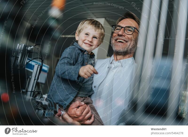Glücklicher Wissenschaftler Vater trägt Sohn, während er im Labor in der Fabrik steht Farbaufnahme Farbe Farbfoto Farbphoto Innenaufnahme Innenaufnahmen innen