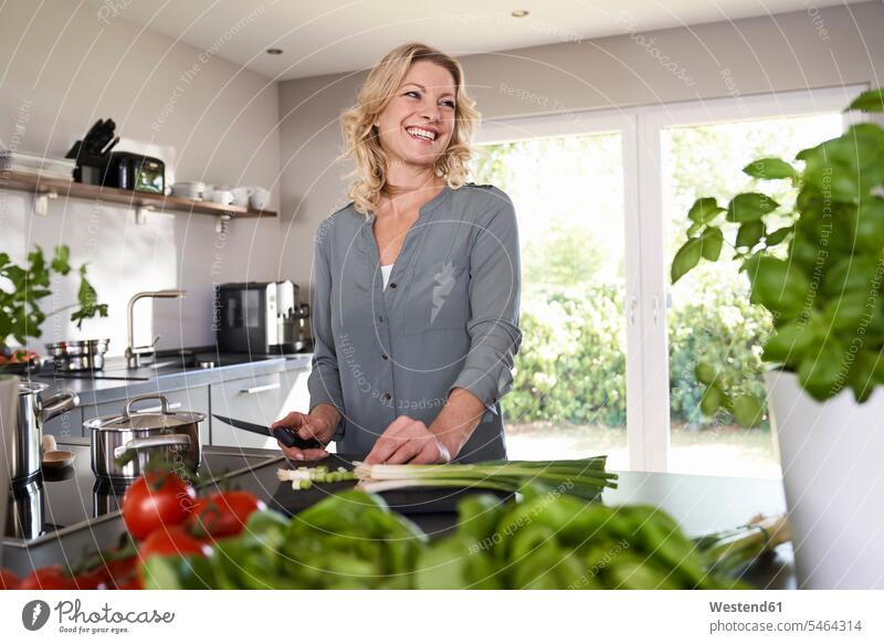Lächelnde Frau schneidet Frühlingszwiebeln in der Küche schneiden Küchen Lauchzwiebel Lauchzwiebeln weiblich Frauen lächeln Gemüse Gemuese Essen Food