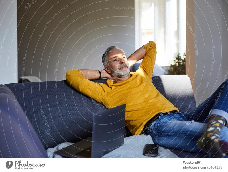 Reifer Mann entspannt sich zu Hause auf der Couch Leute Menschen People Person Personen Alleinstehende Alleinstehender Singles Unverheiratete Unverheirateter