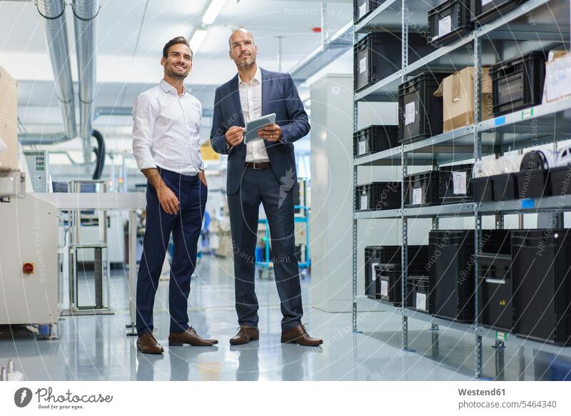 Geschäftsmann hält digitales Tablett in der Hand, während er lächelnd neben einem Ingenieur steht und auf die Fabrik schaut Farbaufnahme Farbe Farbfoto