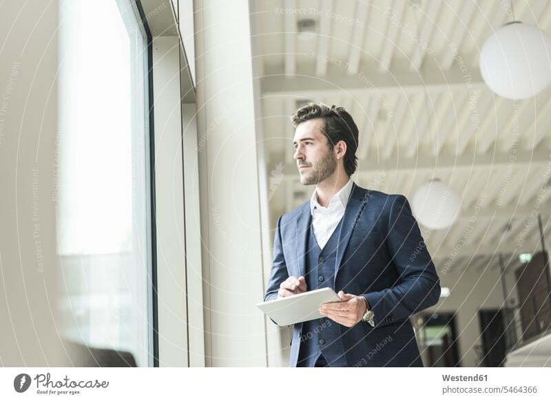 Erfolgreicher Manager steht in einem modernen Bürogebäude, benutzt einen Laptop und schaut aus dem Fenster Job Berufe Berufstätigkeit Beschäftigung Jobs