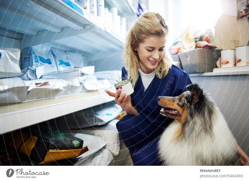 Junge Frau nimmt Futter für einen Hund aus dem Regal in der Tierarztpraxis Tierarztpraxen Hundefutter weiblich Frauen nehmen aufnehmen Ablage Regale