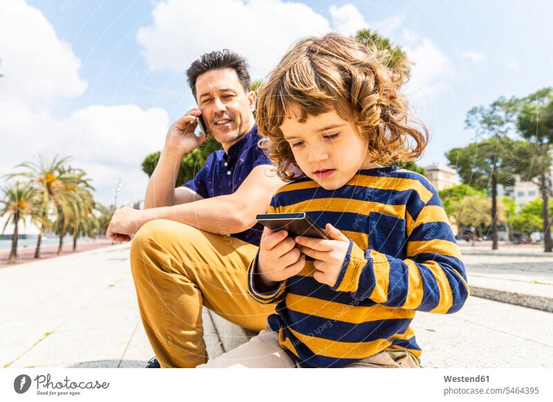 Spanien, Barcelona, Vater und Sohn, beide mit einem Smartphone Söhne Papas Väter Vati Vatis Papis iPhone Smartphones Kind Kinder Familie Familien Mensch