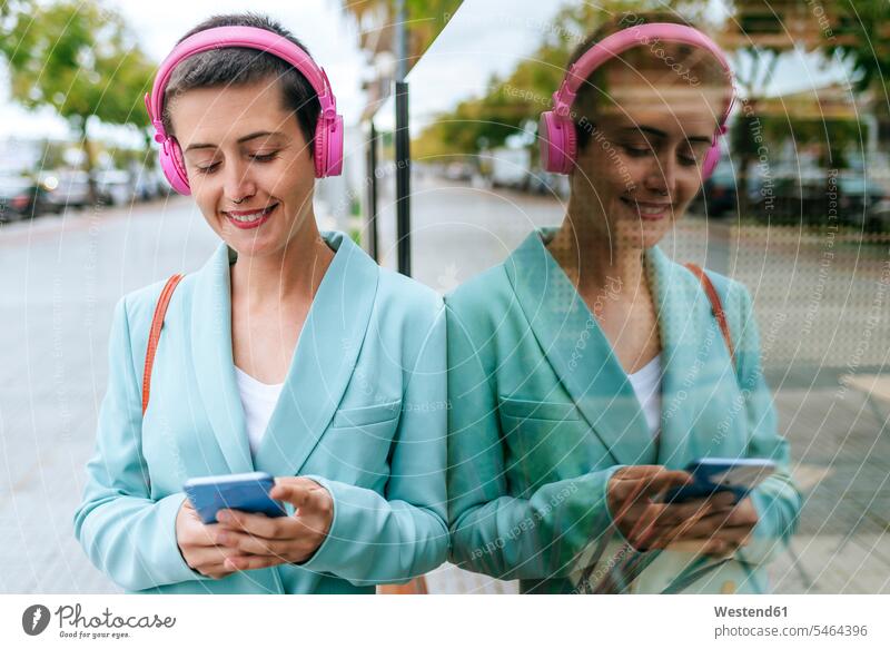 Frau in Jacke, die mit ihrem Handy Musik hört Jackett Anzugjacke weiblich Frauen Smartphone iPhone Smartphones hören hoeren Kopfhörer Kopfhoerer Jacken
