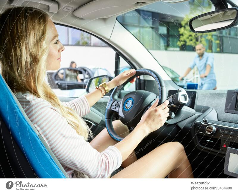 Lächelnde Frau fährt Elektroauto fahren fahrend fahrender fahrendes weiblich Frauen lächeln Elektromobil Elektromobile Elektroautos Auto Wagen PKWs Automobil