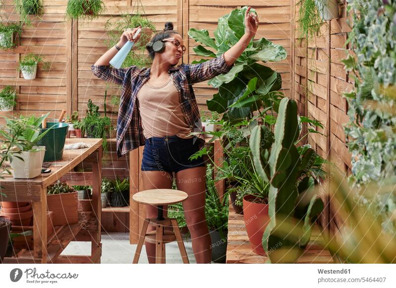 Glückliche junge Frau, die bei der Gartenarbeit auf ihrer Terrasse tanzt Blumentoepfe Blumentöpfe Tische Holztische Kopfhoerer Brillen entspannen relaxen hoeren
