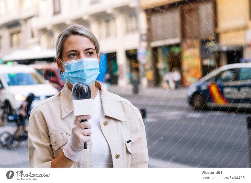 Journalistin, die eine Maske mit Mikrofon trägt und weg schaut, während sie in der Stadt auf der Straße steht Farbaufnahme Farbe Farbfoto Farbphoto Spanien