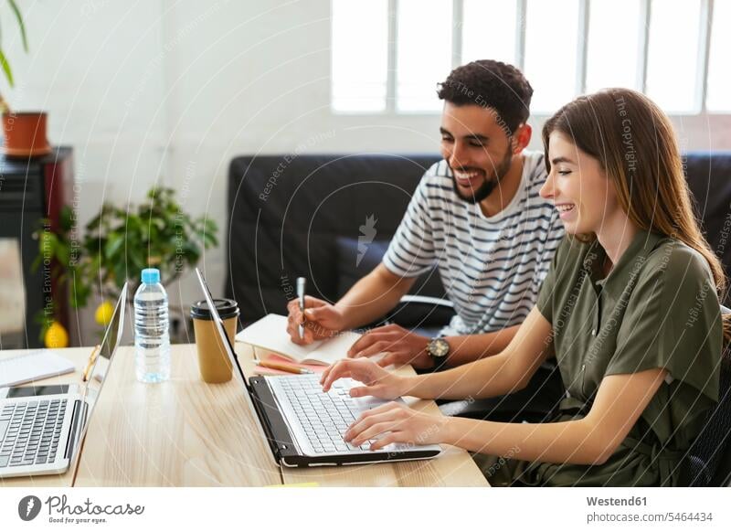 Lächelnde Kollegen arbeiten gemeinsam am Schreibtisch im Büro und teilen sich den Laptop lächeln Office Büros Arbeitskollegen Teilen Sharing Gemeinsam Zusammen