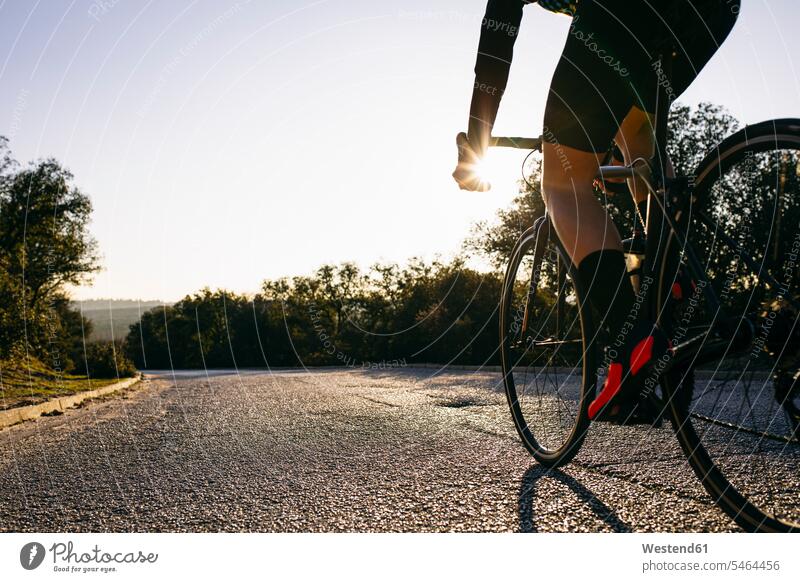 Nahaufnahme eines radfahrenden Athleten auf einer Landstraße bei Sonnenuntergang Raeder Räder Bike Bikes Fahrräder Rad Rennräder fahrender fahrendes abends Muße