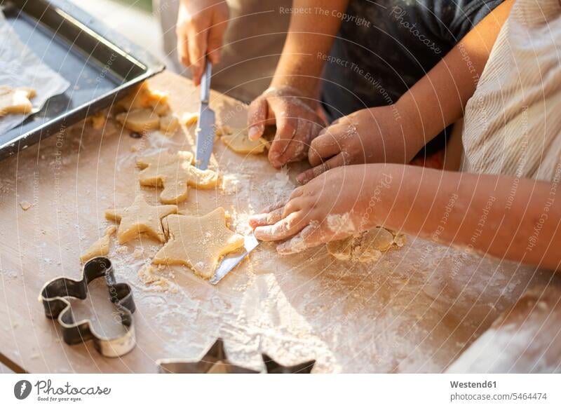 Ausschnittansicht von Kindern, die Kekse ausschneiden Tische Holztische Formen Sterne sternfoermig sternförmig daheim zu Hause Muße Miteinander Zusammen Essen