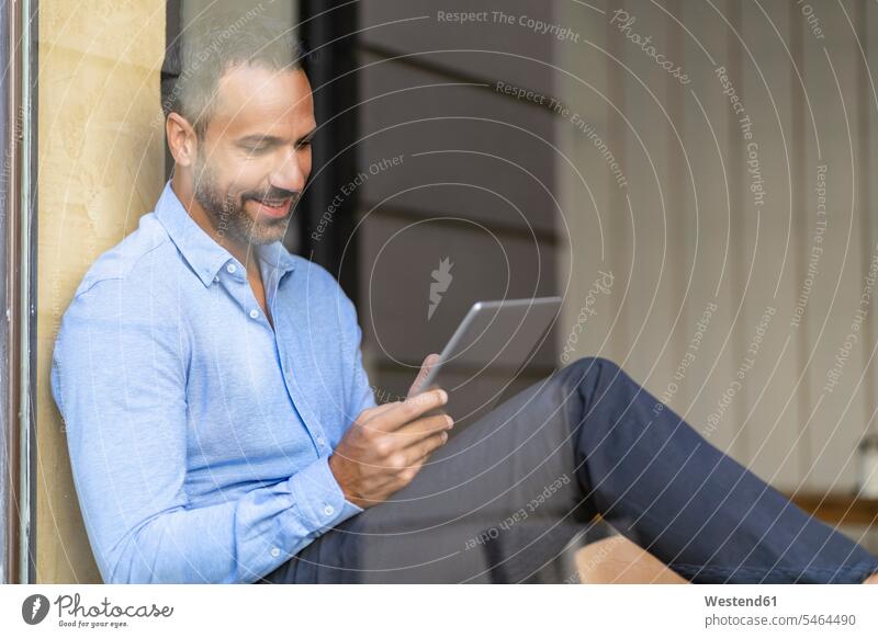 Lächelnde Geschäftsmann sitzt am Fenster mit Tablette Deutschland Spiegelung Spiegelungen Drahtlose Technologie drahtlose Verbindung Drahtlose Kommunikation