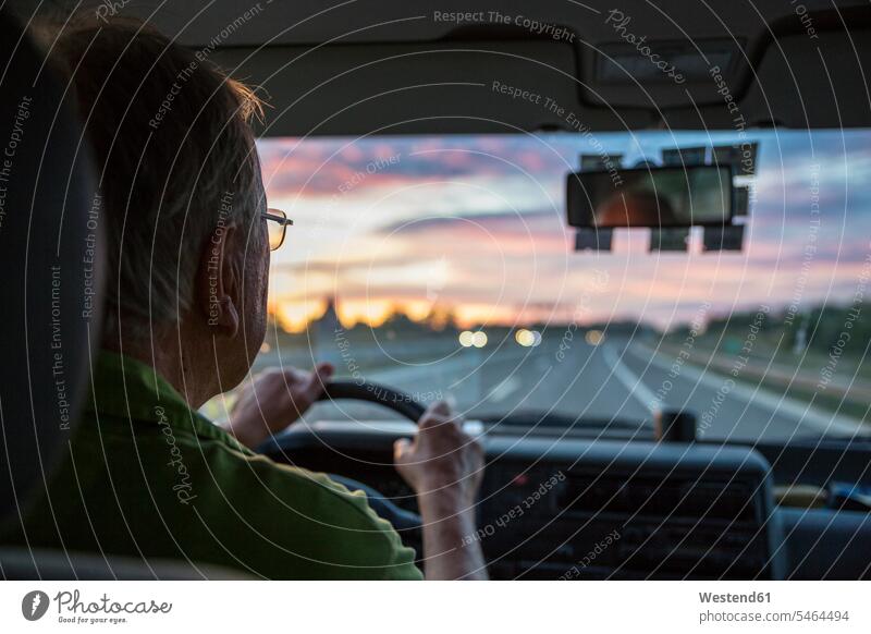 Älterer Mann fährt bei Sonnenuntergang ein Auto auf einer Autobahn Transport Transportwesen KFZ Verkehrsmittel Automobil Autos PKW PKWs Wagen Brillen fahrend