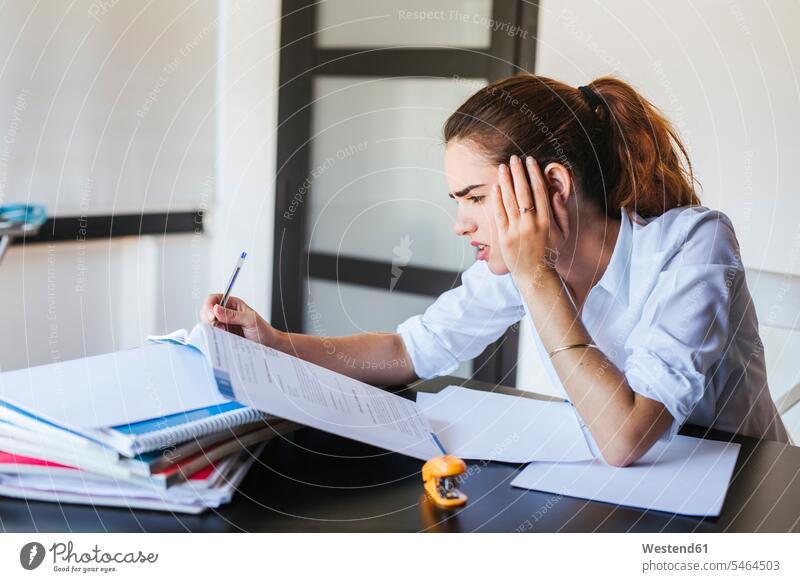 Frustrierte Studentin mit Unterlagen am Schreibtisch zu Hause Tische Arbeitstisch Schreibtische Papiere Stifte Lektüre sitzend sitzt daheim gefühlvoll Emotionen