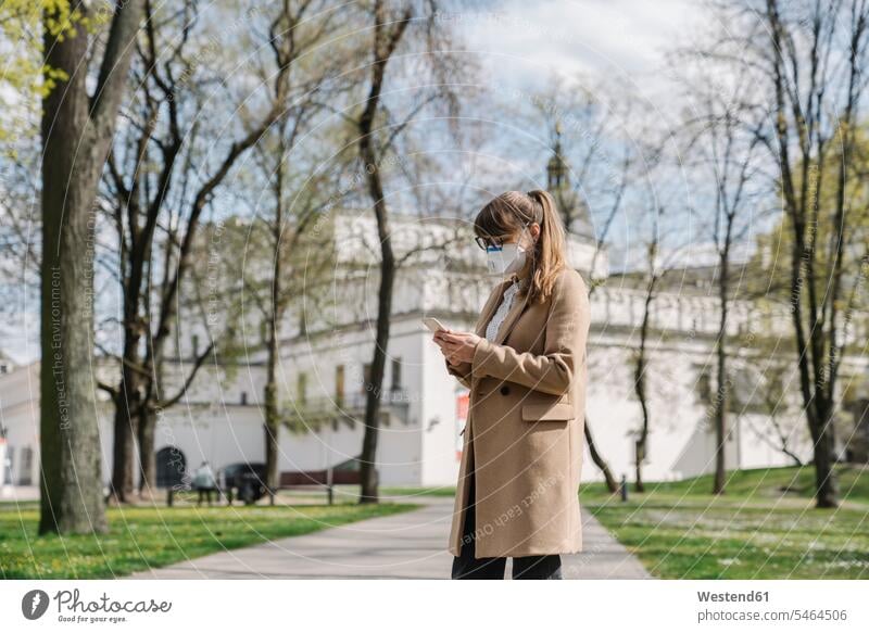Frau mit FFP2-Maske und Smartphone in einem Park Telekommunikation telefonieren Handies Handys Mobiltelefon Mobiltelefone Brillen stehend steht Muße mobil