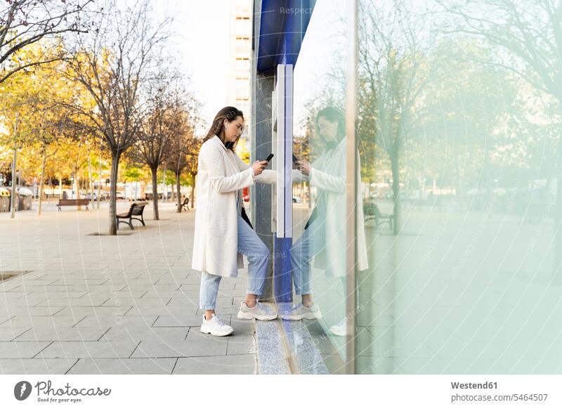 Geschäftsfrau, die Geld am Geldautomaten abhebt, während sie auf einem Fußweg in der Stadt steht Farbaufnahme Farbe Farbfoto Farbphoto Außenaufnahme außen