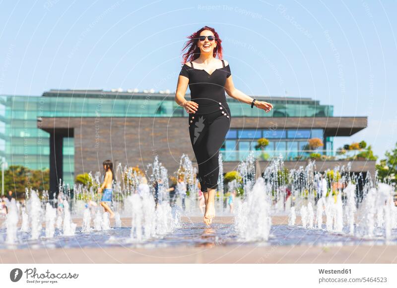 Junge Frau amüsiert sich beim Laufen durch einen Springbrunnen laufen rennen Spaß Spass Späße spassig Spässe spaßig weiblich Frauen Brunnen Erwachsener