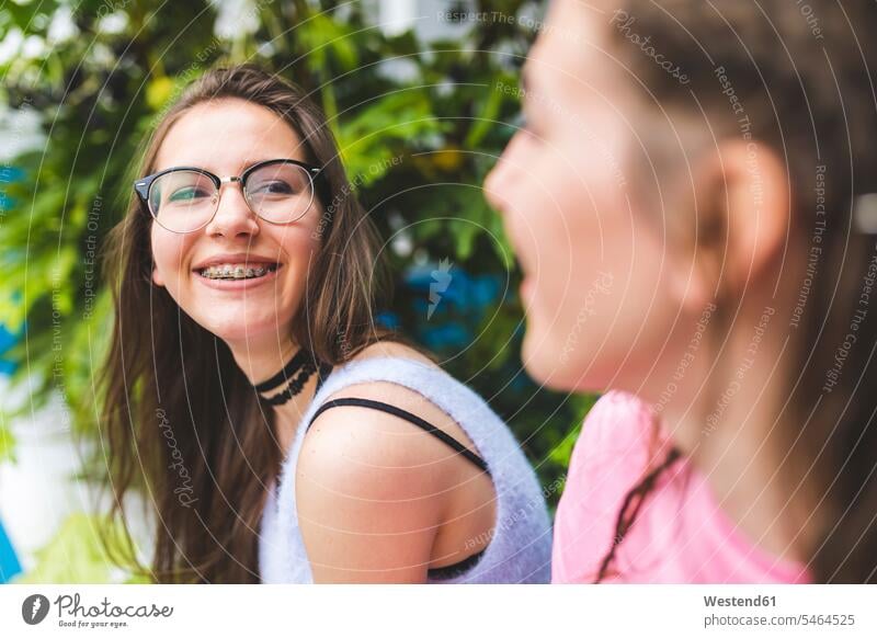 Glückliches Teenager-Mädchen mit Zahnspange und Brille schaut Freundin an Freundinnen ansehen Zahnspangen Zahnklammer Zahnklammern Teenagerin junges Mädchen