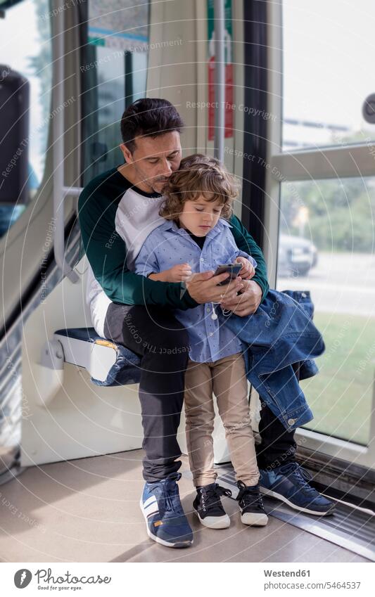Vater und Sohn benutzen Handy in einer Straßenbahn Papas Väter Vati Vatis Papis Trambahn S-Bahn S-Bahnen Strassenbahnen Straßenbahnen Mobiltelefon Handies