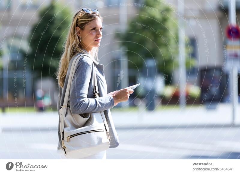Junge Geschäftsfrau, die mit einem digitalen Tablet arbeitet, während sie mit einem Koffer auf der Straße steht geschäftlich Geschäftsleben Geschäftswelt