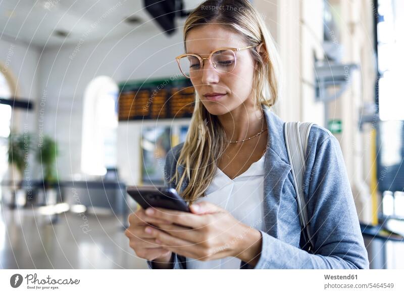 Junge Frau schreibt mit ihrem Mobiltelefon in der Bahnhofshalle geschäftlich Geschäftsleben Geschäftswelt Geschäftsperson Geschäftspersonen Businessfrau