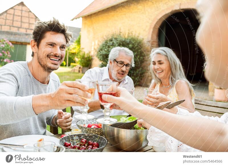 Glückliche Familie beim gemeinsamen Essen im Garten, mit Gläsern anstoßen Deutschland Lebensqualität Quality Time Geselligkeit gesellig Freunde Tischdekoration