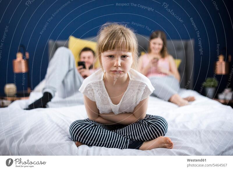Wütendes kleines Mädchen, das mit seinen Eltern im Bett sitzt verärgert missmutig aergern veraergert mürrisch muerrisch ärgern Betten Langeweile langweilig