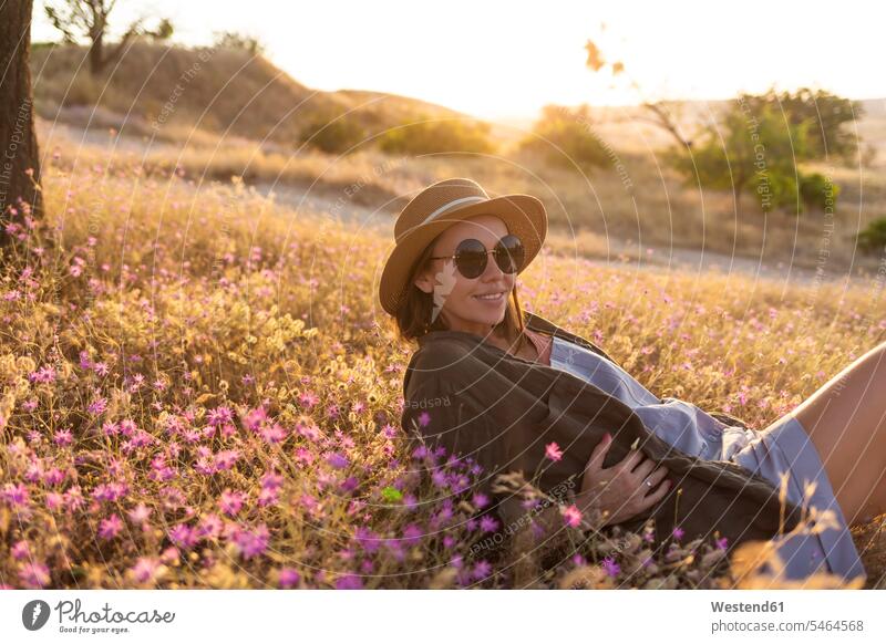 Junge Frau liegend auf Wiese bei Sonnenuntergang Brillen Sonnenbrillen sitzend sitzt abends entspannen relaxen entspanntheit relaxt freuen geniessen Genuss
