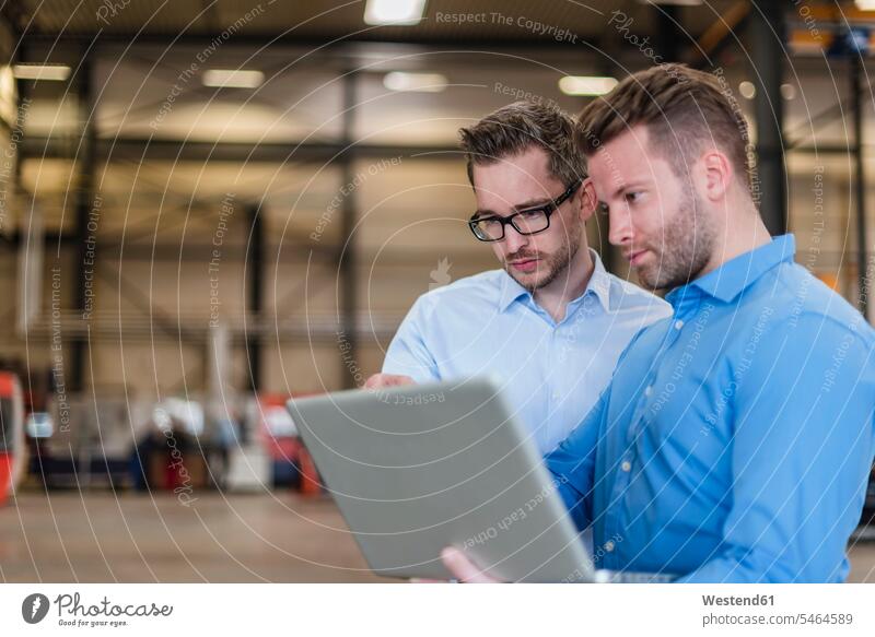 Zwei Geschäftsleute teilen sich einen Laptop in der Fabrikhalle Kollegen Arbeitskollegen Teilen Sharing Notebook Laptops Notebooks Produktionshalle Montagehalle