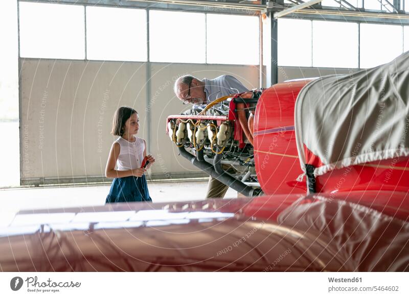 Großvater konzentriert sich, während er im Hangar stehend zeigt, wie man ein Flugzeugwerkzeug an seiner Enkelin befestigt Farbaufnahme Farbe Farbfoto Farbphoto