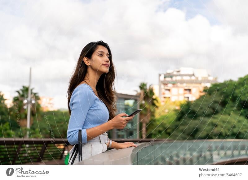 Nachdenkliche Geschäftsfrau hält Mobiltelefon in der Hand, während sie auf der Fußgängerbrücke steht Farbaufnahme Farbe Farbfoto Farbphoto Spanien Außenaufnahme