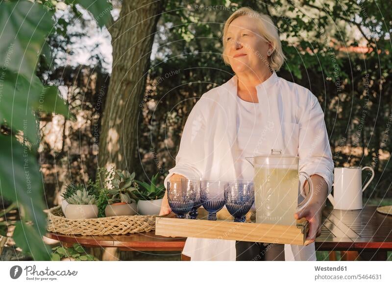 Nachdenkliche ältere Frau trägt Tablett mit Getränken, während sie im Hof steht Farbaufnahme Farbe Farbfoto Farbphoto Spanien Freizeitbeschäftigung Muße Zeit