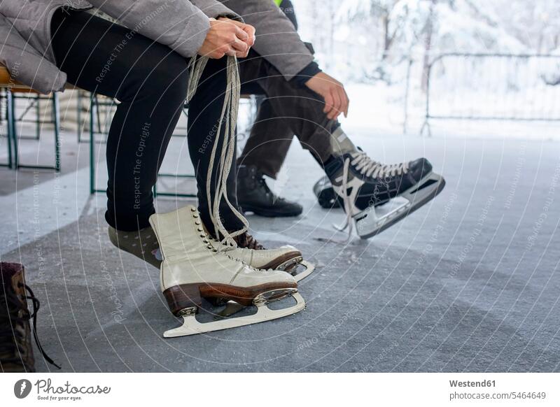 Paar sitzt auf einer Bank an der Eisbahn und zieht Schlittschuhe an Pärchen Paare Partnerschaft anziehen anlegen Bein Beine sitzen sitzend Schlittschuhlaufen