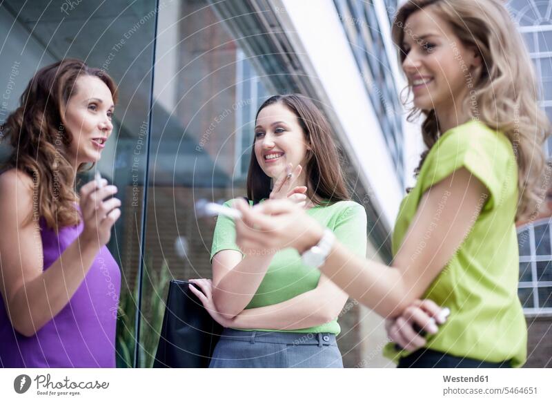 Weibliche Kollegen tratschen während des Zigarettenrauchens in der Pause vor dem Büro Farbaufnahme Farbe Farbfoto Farbphoto Außenaufnahme außen draußen