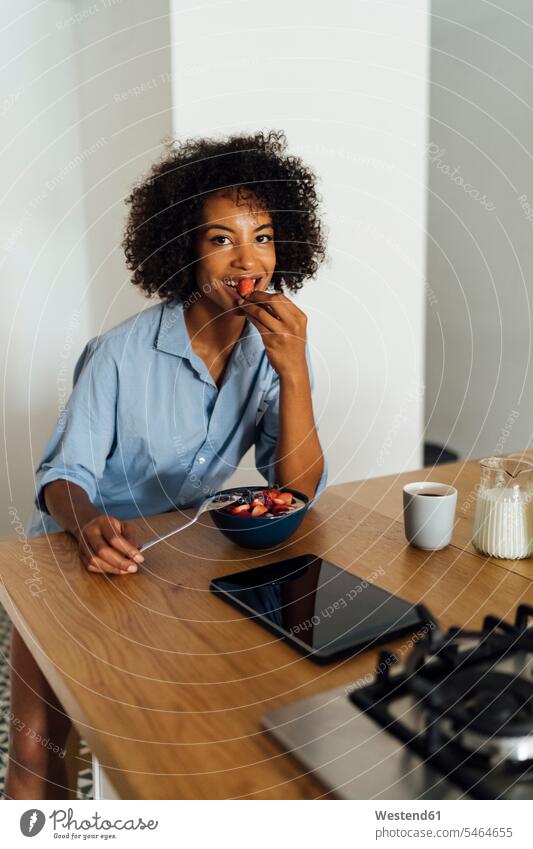 Frau mit digitalem Tablet und mit einem gesunden Frühstück in ihrer Küche morgens Morgen früh Frühe sitzen sitzend sitzt lächeln Küchen benutzen benützen Obst