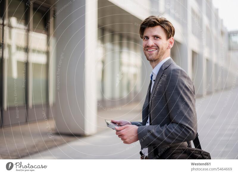 Lächelnder Geschäftsmann in der Stadt mit Tasche und Tablet Businessmann Businessmänner Geschäftsmänner Tablet Computer Tablet-PC Tablet PC iPad Tablet-Computer