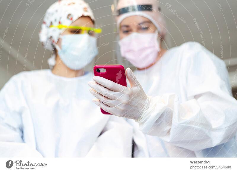 Zahnarzt zeigt der Assistentin sein Mobiltelefon im Stehen im Büro Farbaufnahme Farbe Farbfoto Farbphoto Innenaufnahme Innenaufnahmen innen drinnen Tag