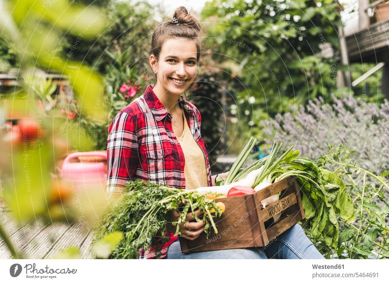 Lächelnde schöne Frau mit Gemüsekiste im Gemeinschaftsgarten sitzend Farbaufnahme Farbe Farbfoto Farbphoto Deutschland Freizeitbeschäftigung Muße Zeit