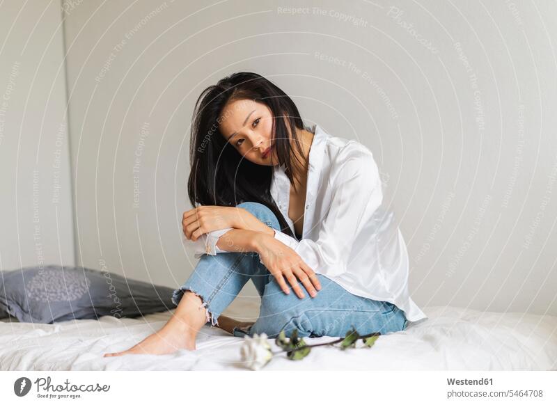 Porträt einer attraktiven jungen Frau auf dem Bett sitzend mit weißer Rose weißes weiss schoen gut aussehend schön Attraktivität gutaussehend hübsch Betten