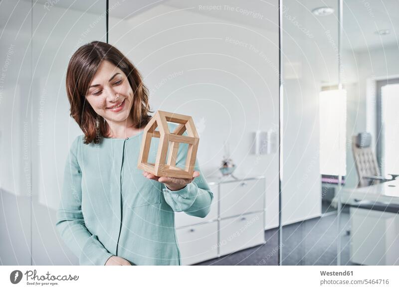 Lächelnde junge Geschäftsfrau betrachtet Architekturmodell im Büro Portrait Porträts Portraits Office Büros Geschäftsfrauen Businesswomen Businessfrauen