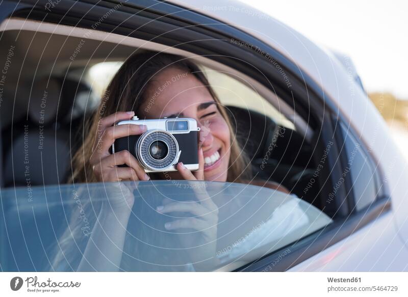 Frau sitzt im Auto und fotografiert mit einer Kamera junge Frau junge Frauen Ausflug Ausflüge Kurzurlaub Ausfluege Kameras fotografieren Wagen PKWs Automobil