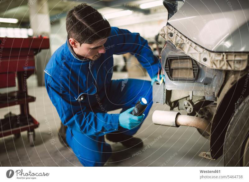 Mechaniker, der in einer Werkstatt ein Auto mit einer Taschenlampe inspiziert Monteur Wagen PKWs Automobil Autos Taschenlampen inspizieren prüfen untersuchen