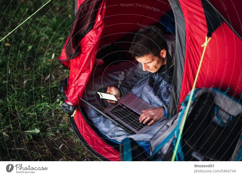 Mann zeltet in Estland, sitzt im Zelt, benutzt Laptop Notebook Laptops Notebooks Zelte Natur zelten Camping Campen Computer Rechner reisen Travel verreisen Weg