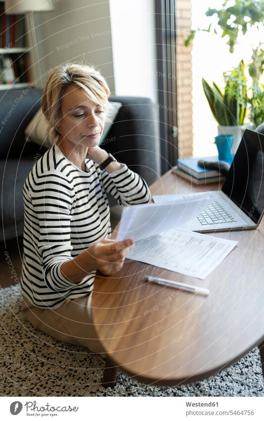 Reife Frau mit Dokumenten, die zu Hause einen Laptop benutzen Leute Menschen People Person Personen Alleinstehende Alleinstehender Singles Unverheiratete