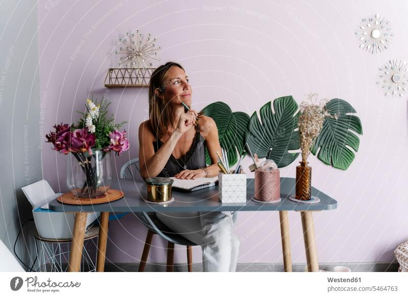 Nachdenkliche Frau schaut weg, während sie mit dem Tagebuch am Tisch an der Wand sitzt Farbaufnahme Farbe Farbfoto Farbphoto Spanien Innenaufnahme
