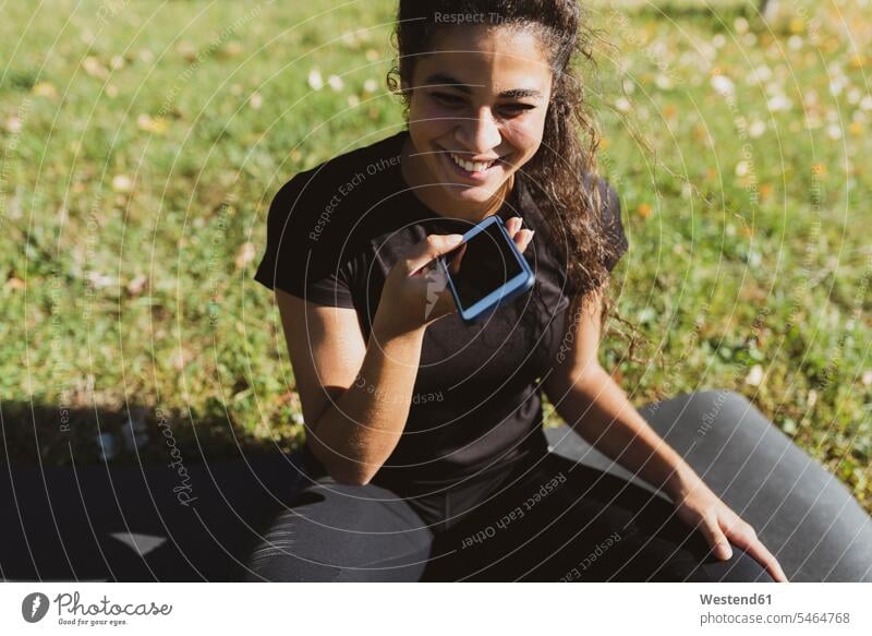 Glückliche sportliche junge Frau, die eine Pause auf einer Wiese mit Handy Wiesen Mobiltelefon Handies Handys Mobiltelefone weiblich Frauen Sport Telefon